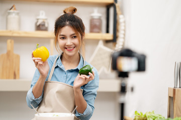 Young asian woman blogger or vlogger looking camera, showing raw material and sharing tutorial  for cooking vegetarian saladon video shooting with technology. Social media influencer content concept.