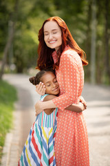 Wall Mural - Beautiful red-haired woman smiling while hugging daughter