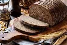 Sliced Rye Bread On A Rustic Cutting Board With Grain And Rye Ears At The Background