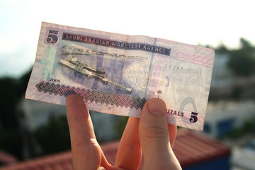 A man holding 5 saudi riyal in his hand. Saudi Arabia currency.