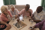 Group of senior people playing chess in living room