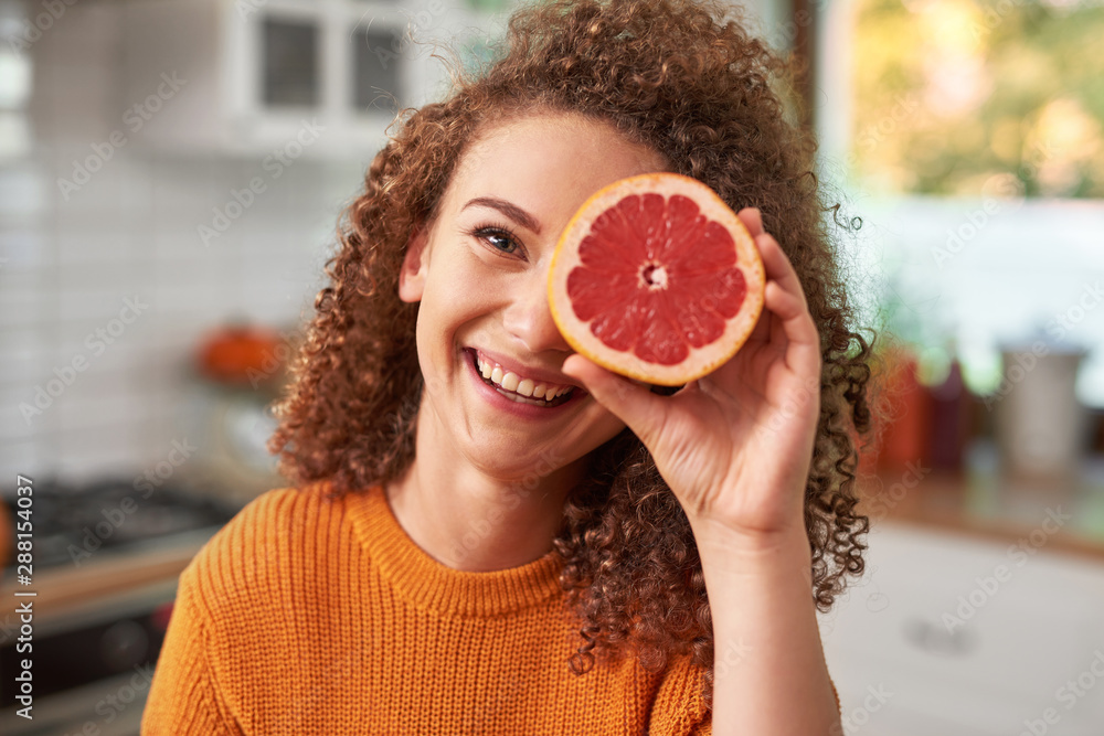 Portrait of woman covering her eye with grapefruit - obrazy, fototapety, plakaty 