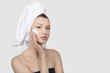 © Alena - Portrait of a young woman with cream on her face. hand touch to the cheek. A towel on her head. White background