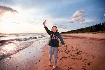 Wall Mural - happy excited young boy having fun on a sandy autumn beach, raising up victory sign fingers