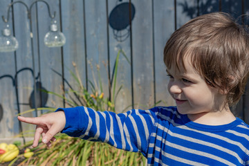 An adorable little boy, a toddler of about two years of age, reaches out to happily point at something.