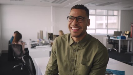 Wall Mural - Portrait of a young african corporate businessman laughing at workplace in front of colleagues working at background