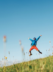 Wall Mural - backpacker traveler emotionally jumping over green grass mountain meadow with backpack with wide ope