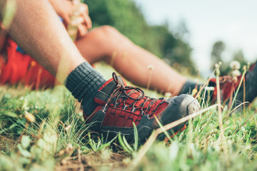 Wall Mural - backpacker's trekking boots close up shot. man has a rest break sitting on green grass and enjoying 