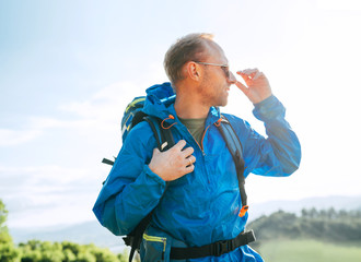 Wall Mural - backpacker man lifestyle side portrait enjoying mountain landscape. he wears in blue rain coat ponch