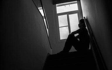 Wall Mural - Silhouette of a sad man Sitting at the stairs in the dark leaning against the wall with his back, The sun is in sorrow.