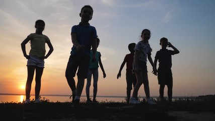 Poster - Silhouettes of cute little children near river at sunset, slow motion. Outdoor play