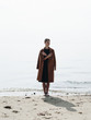 © Alina Hvostikova/Stocksy - Barefoot woman in coat near sea
