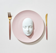 Serving Diner Place With Plaster Mask On A Plate, Fork, Knife Isolated On A Light Background, Copy Spase. Top View. Cosmetology Concept.