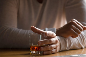 Close up man holding glass with alcohol in hand, drinking alone