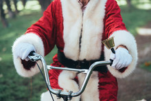 Unrecognizable Crop Person In Costume Of Santa Claus Sitting On Cycle, Ringing Bell And Looking At Camera