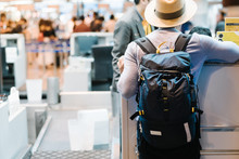 Attractive, Handsome And Stylish Man, With Short Brim Hat, Talks And Waits For Check In At Airline Counter, Stand And Carry Backpack At Departure Airport Terminal For His Leisure Vacation / Journey.