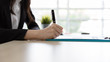Close up Hand of Businesswoman signs, writing the documents on in desk at office building with natural light. Contracts and business agreements
