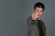 © artit - Short haired men wear dark green shirts, using the index finger standing on a gray background.