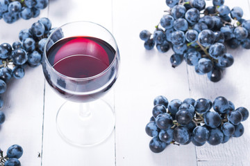 Wall Mural - glass of red wine and blue grapes on white wooden table background