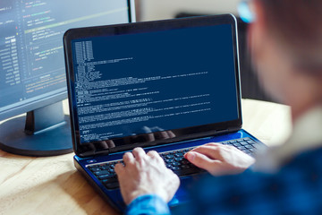 Wall Mural - back view of man freelancer is working on laptop at home office. programmer developer is writing pro