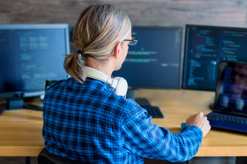 Wall Mural - back view of man freelancer in white headphones is working at home office. programmer developer is w