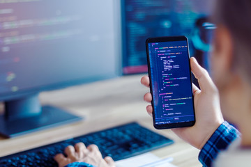 Wall Mural - closeup freelancer hand is holding smartphone with program code. programmer developer is writing sof