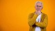 Senior man touching chin, thinking about decision against orange background