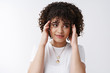 © Cookie Studio - Stylish silly curly-haired female student smiling look away touching head temples feel pressured brain gonna explode loads information willing have fun relax mid-term exams bother, white background