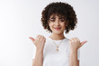 © Cookie Studio - Pick your way. Friendly-looking assertive stylish curly-haired female pointing thumbs left right sideways giving variants promoting product grinning satisfied found perfect places customer