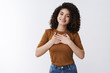 © Cookie Studio - Girl feel grateful thanks bottom heart. Attractive cheerful curly-haired modern young woman hold hands chest thankful smiling pleased like touching cute gift standing white background appreciate