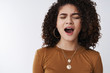 © Cookie Studio - Boring. Bored uninterested sleepy attractive modern 20s curly-haired mixed race female yawning open mouth wide close eyes frowning falling asleep partying all night wanna nap need coffee