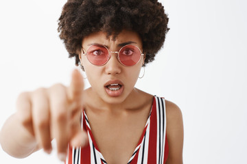 Wall Mural - Bothered woman staring at something confusing, pointing at camera while being questioned and clueless, opening mouth and frowning, feeling intense and unsure what she sees over gray background