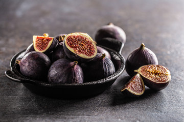 A few figs in a black bowl on an dark concrete table