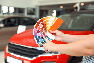 Poster - Young woman holding palette with color samples near modern car, closeup