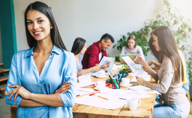 Wall Mural - Attractive confident modern business woman in casual clothes looks at the camera and smiling. Modern start-up business team. Co-workers or students 