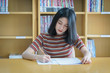 © EduLife Photos - Young female university student concentrate doing language practice examination inside library. Girl student writes the exercise of the examinations. University examination and education concept.