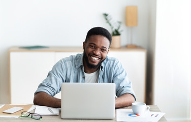 Wall Mural - Smiling businessman sitting at workplace in modern office and laughing