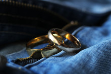 Two Gold Wedding Rings On Blue Jeans. The Concept Of Love Or Marriage.