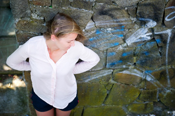 young woman in a white shirt stands near a painted wall and looks away