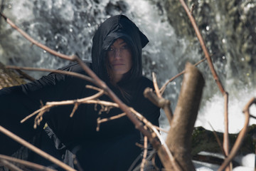 Hooded Woman in black robes in front of the Waterfall. Witches. Halloween and Gothic concept. Witchcraft and magic.