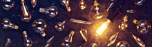 Vintage Old Light Bulb Glowing Yellow On Rough Dark Background Surrounded By Burnt Out Bulbs. Idea, Creativity Concept.