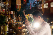 Faith And Religious. .Man Hands Holding Joss Sticks Praying And Blessing In Front Of Altar Table At Chinese Shrine With Blurred Gods Statue In Background.