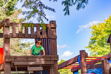 A Little Boy, About 2 Years Old, Looks Down From The High Platform On A Wooden Play Structure.
