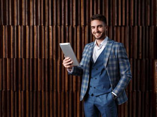 young successful businessman with a beard in a luxurious blue checked suit. Man works on a tablet in a loft office