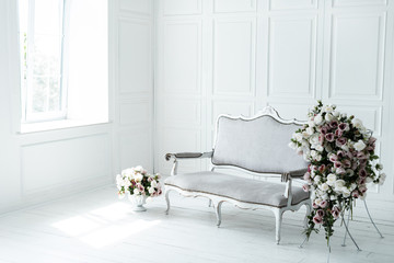 Antique light sofa in front of a white wall near the window, artificial flowers in the interior