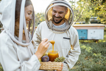 Beekepers in protective uniform standing with fruits and honey in the jar, tasting fresh product on the apiary outdoors