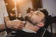 © romaset - Young man with trendy haircut at barber shop. Barber does the hairstyle and beard trim.
