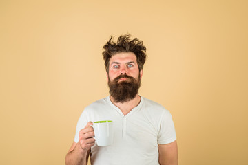 Sleepy guy with cup of tea or coffee. Morning with coffee or milk. Man with sleepy face try to awake with cup of coffee. Sleepy man with beard holds mug in hand. Morning coffee. Breakfast concept.