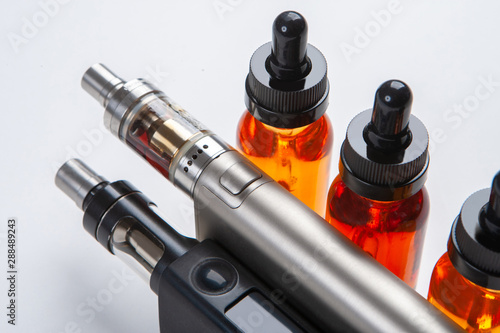 Silver and black vapes next to the vials. Liquids for electronic cigarettes. Smoking e-cigarettes. Vaping accessories. Devices for Smoking electronic cigarettes.