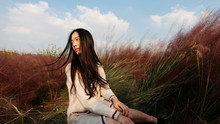 Portrait Of Beautiful Young Chinese Woman Wearing White Sweater Dress Sitting In The Pink Hairawn Muhly Field, Shaking Her Head Enjoy The Wind.